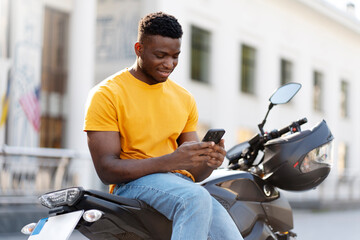 smiling african american man using mobile phone while relaxing at the street