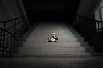 Lonely teddy bear on grey stairs indoors