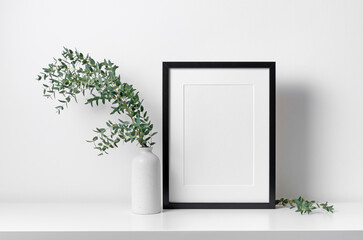 Wall Mural - Portrait blank frame mockup in white interior with eucalyptus plant decoration