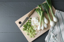 Board with knife, whole and cut spring onions on grey wooden table, flat lay. Space for text