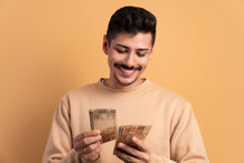 Happy Brazilian Man Looking At Brazilian Money Cash In Beige Studio Background. Financial, Credit, Purchase, Rich Concept. 