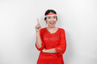 Excited Asian woman wearing red kebaya and flag headband, pointing at the copy space on top of her, isolated by white background