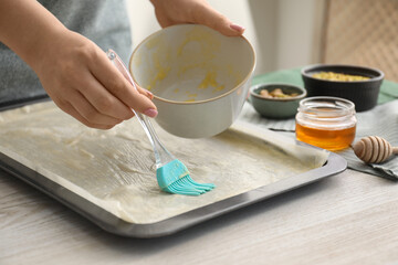 Making delicious baklava. Woman buttering dough in baking pan at white wooden table, closeup