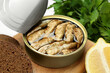 Canned sprats, lemon and bread on wooden board, closeup