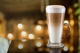 Glass mug of latte coffee on the bar counter with blurred background. Copy space.