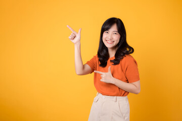 Radiate joy with a young Asian woman in her 30s, wearing an orange shirt, pointing to free copy space on yellow background. recommending product concept.