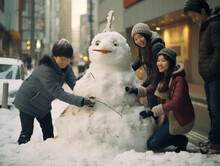 Asian People In Warm Clothes, Scarves And Hats Making Snowman Together In Winter