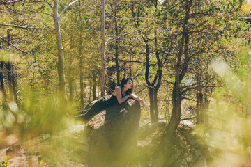 Beautiful woman lies on a rock cliff in the forest enjoying a warm sunny day.