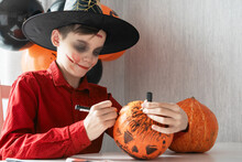 Teen Boy In Costume Drawing Coronavirus Image On The Pumpkin For The Halloween Celebration. Halloween Carnival With New Reality With Pandemic Concept.