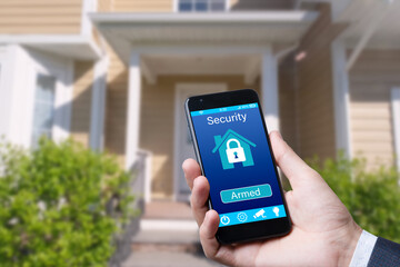 Poster - Smartphone with home security app in a hand on the building background.
