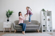 © sofiko14 - Full length view of smiling lady in jeans supporting cute girl in testing great bounce of cushiony couch in family lounge. Delighted mom-daughter duo experiencing feeling of freedom and well-being.