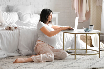 Wall Mural - Young pregnant woman working with laptop in bedroom