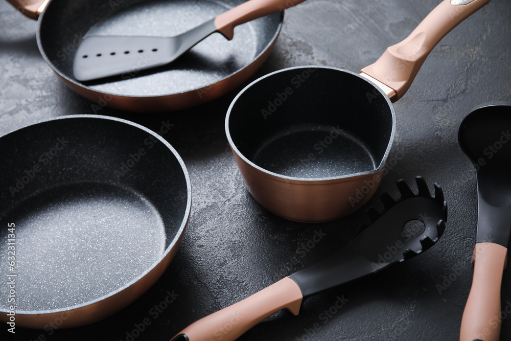 Cooking pots, frying pan and kitchen utensils on dark background, closeup