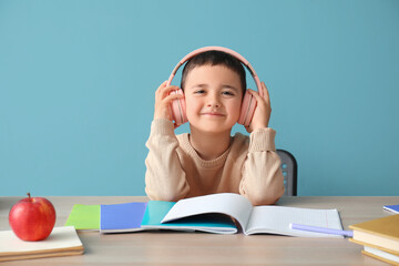 Poster - Cute little boy in headphones doing homework at table near blue wall