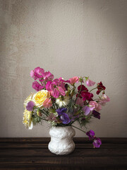 Beautiful flowers in vase on moody rustic background. Stylish flowers still life, artistic composition of lathyrus, love in the mist, rose. Floral vertical wallpaper