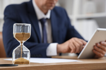 Canvas Print - Hourglass on table of mature businessman in office, closeup