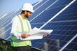 © Serhii - Portrait of Young indian man technician wearing white hard hat standing near solar panels against blue sky.Industrial worker solar system installation, renewable green energy generation concept.