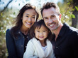 Casual close-up portrait of mixed-race family of white father, asian mother, and biracial daughter. All are looking at the camera and smiling.