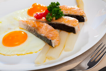 Wall Mural - Hearty breakfast of fried eggs with salmon and steamed asparagus garnished with tomatoes and fresh greens..