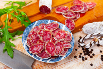 Wall Mural - Sliced spanish sausage fuet on a ceramic plate with kitchen knife on a wooden background