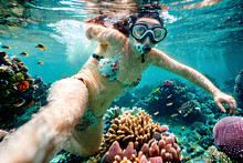 A Young Woman Wearing Snorkeling Mask Swims Playfully In The Sea As She Looks At The Camera And Invite Us To Explore An Underwater World Rife With Colorful Coral Reef And Marine Life. Generative AI.