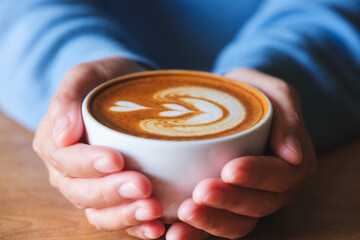 Canvas Print - Closeup image of a woman holding a cup of latte coffee on wooden table