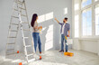 © Studio Romantic - Couple decorating room and painting walls together in their new home. Happy husband and wife with paint rollers renovating their house. Couple standing and discussing color of walls
