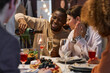 © Seventyfour - Happy young African American man pouring red wine into flute of his girlfriend while sitting next to her by served table at home party