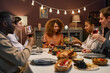 © Seventyfour - Group of young intercultural men and women sitting by served festive table, communicating and having homemade food and drinks