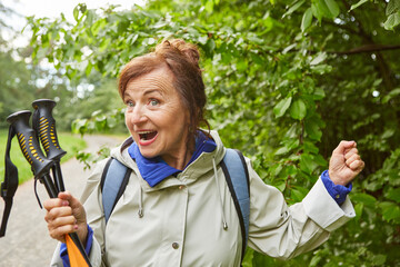 Wall Mural - Cheerful senior woman with hiking poles wearing jacket