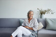 © uv_group - Smiling middle aged woman sitting on sofa at home, single mature senior in living room