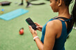 © Lumos sp - Portrait of a young black woman using a phone and texting taking a break exercising in a gym, having a training workout in gym, healthy lifestyle and cardio exercise at fitness club concepts