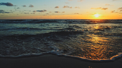 Poster - Beautiful sandy beach while sunset. Beautiful seascape of a sandy beach. Sun over horizon and  rolling ocean waves to the shore while sunset. Summer, travel and tourism. Beautiful wild nature.