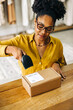 © (JLco) Julia Amaral - Young black woman using a barcode scanner to process a package for dropshipping