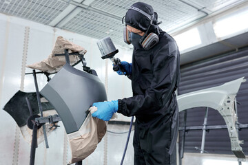 The car's parts receive a professional makeover as a technician, clad in a black jumpsuit, paints in a controlled chamber.