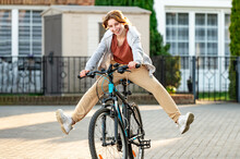 Funny Girl Riding A Bike In The Evening In A Calm City. Young Girl Joking And Having Fun. Eco-friendly Urban Transport.