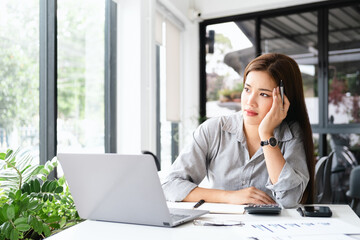 Wall Mural - Young thoughtful Asian business woman executive manager wearing shirt working in modern office, taking notes and thinking of professional plan, project management, considering new business ideas.