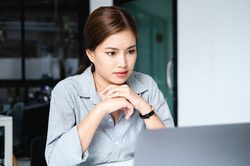 Wall Mural - Millennial Asian businesswoman focusing on her project assignment, using laptop computer, working in her office room.