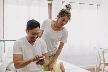 Wall Mural - Funny asian couple. Wife peeking husband who chatting on the smartphone.