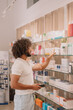 © ADDICTIVE STOCK - Black man with afro hairstyle holding smartphone and reading label on bottle at pharmacy