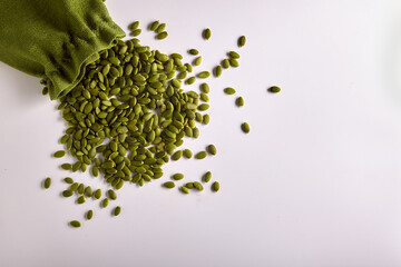 Wall Mural - Pumpkin seeds on a white background in a storage bag, top view. Peeled raw healthy pumpkin seeds are poured out of a green bag. Healthy snack from healthy food