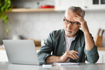 Planning Concept. Pensive Senior Man Using Laptop And Writing In Notebook