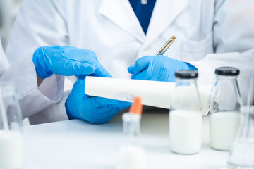 Wall Mural - Food scientist testing new stuff samples of dairy products in the laboratory, female laboratory assistant checks a quality of milk, bottles glassware and glasses of milk to testing lactose forms