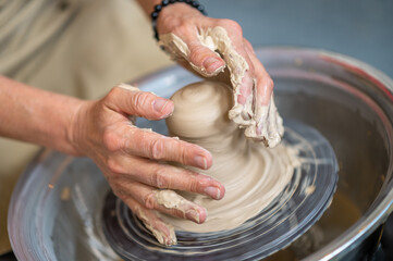 Woman working on potter's wheel in a pottery workshop, creating clay pot.