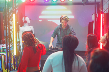Man dj performing using electronic music mixer and laptop on stage in nightclub. Musician in headphones playing at concert in dark club with spotlights at discotheque party