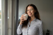 © Miljan Živković - one caucasian woman hold cup of coffee while stand at the window