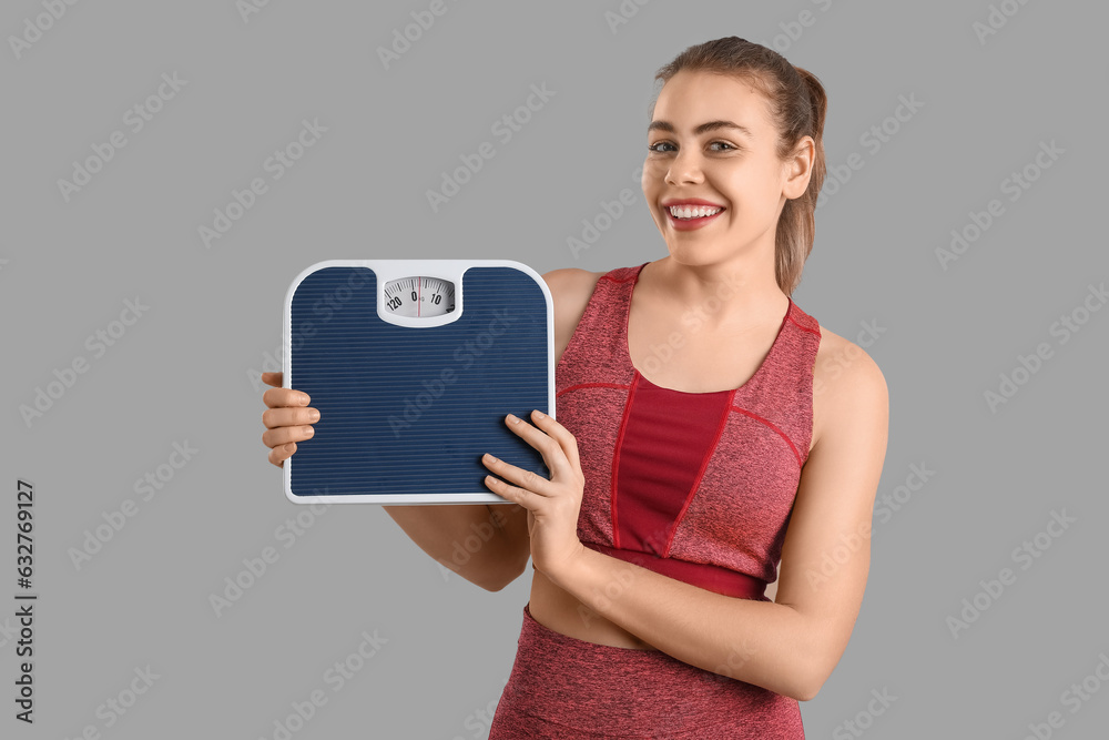 Sporty young woman with scales on grey background