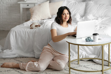 Wall Mural - Young pregnant woman working with laptop in bedroom