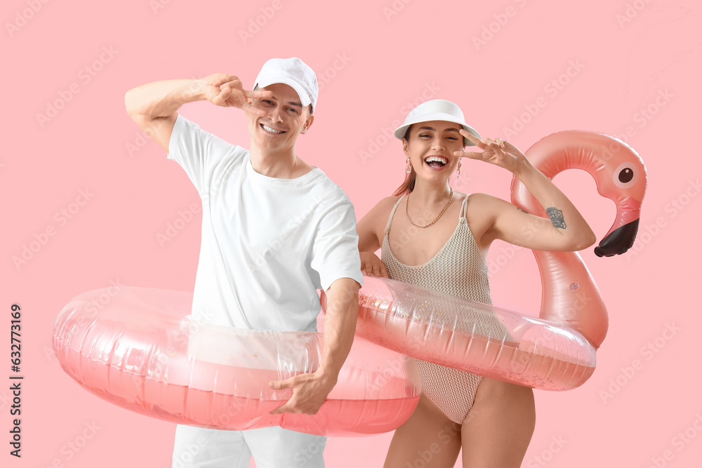 Young couple with inflatable rings showing victory gesture on pink background