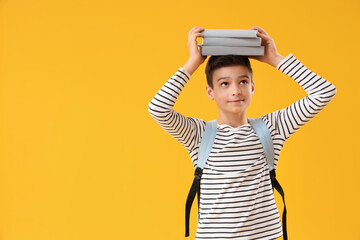 Portrait of schoolboy with backpack holding books on his head against orange background
